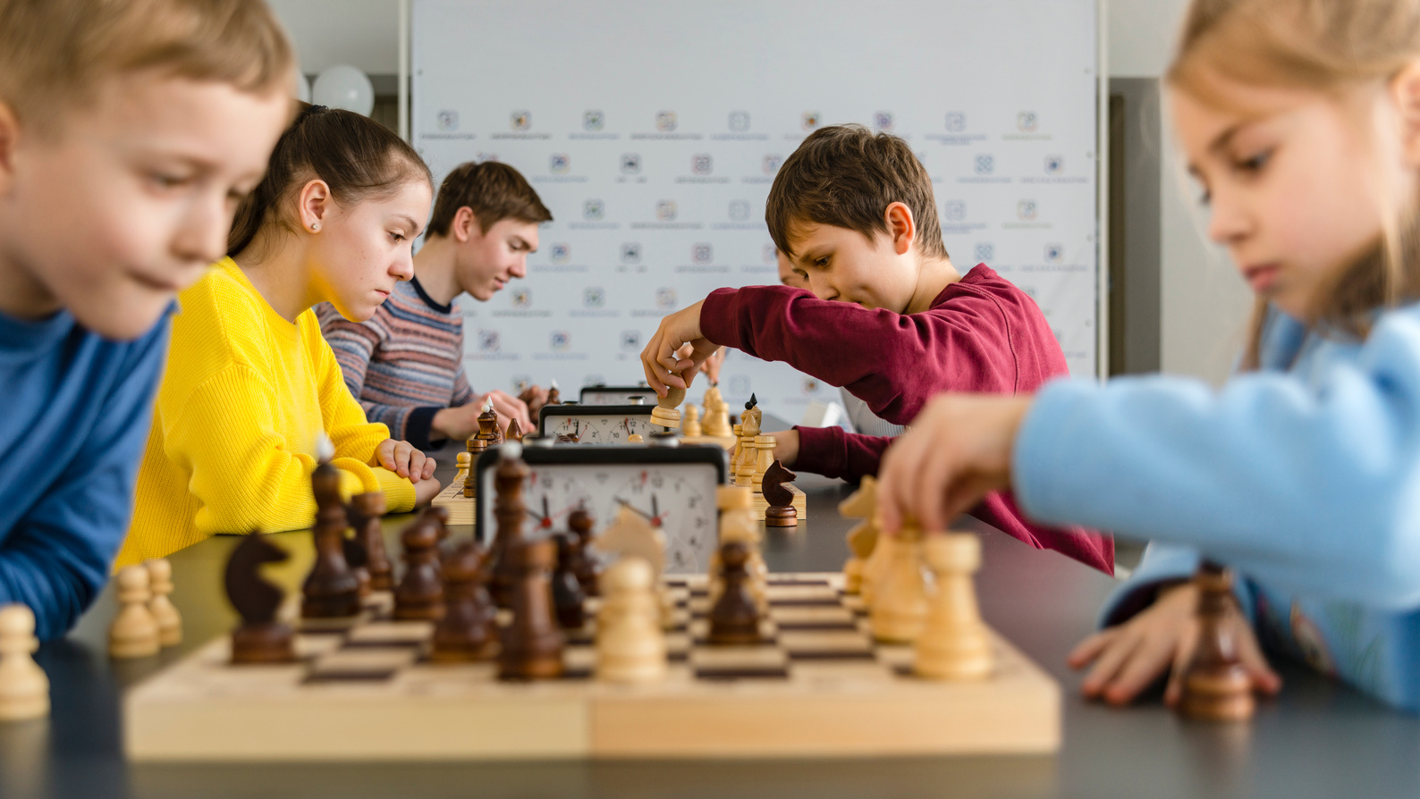 Kids of different ages, boys and girls, playing chess on the tournament in the chess club